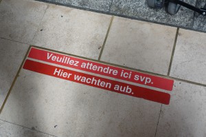 駅の構内にて。「ここでお待ち下さい」という意味のフランス語・オランダ語による表示です。